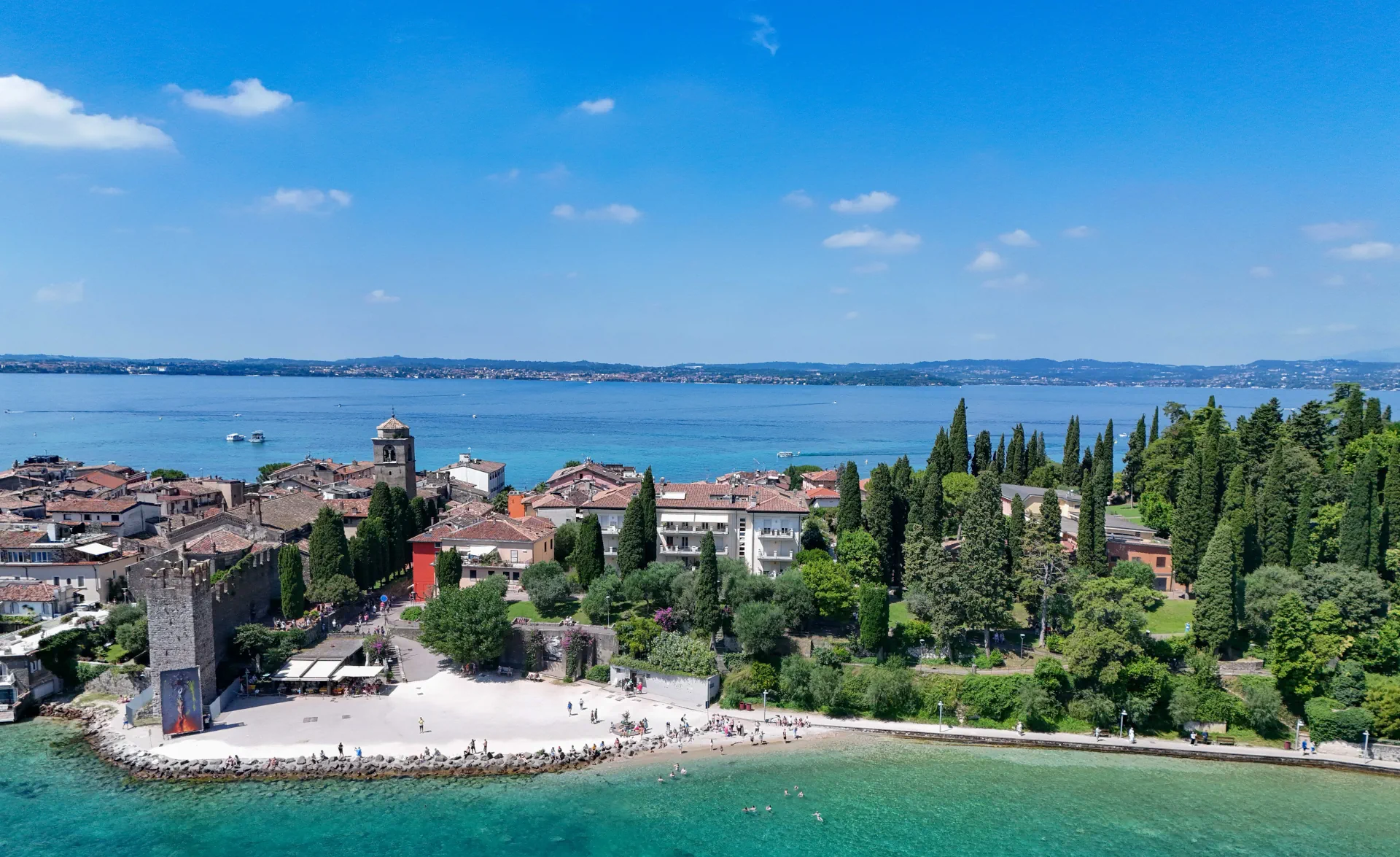 Aerial view of old town of Sirmione with Garda Amore building in the middle, lake and hills in the back.